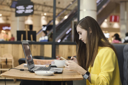 女人喝咖啡,通过手机浏览,用电脑工作. 自由工作照片