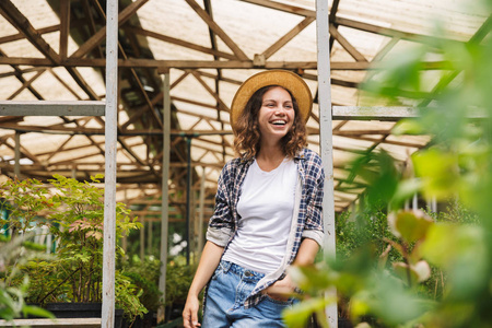 20多岁的年轻花店女士在温室里摆姿势，在植物上工作