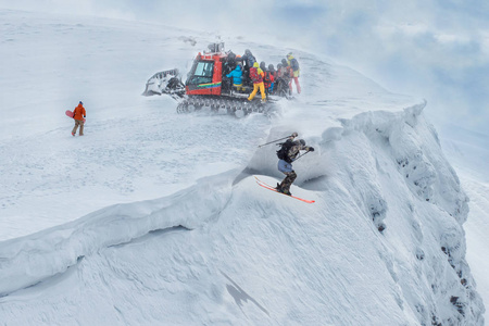 一群自由主义者乘雪车到达山顶。 一个滑雪者跳下悬崖。