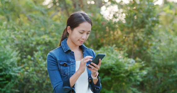 女人在阳光下查看城市公园的手机