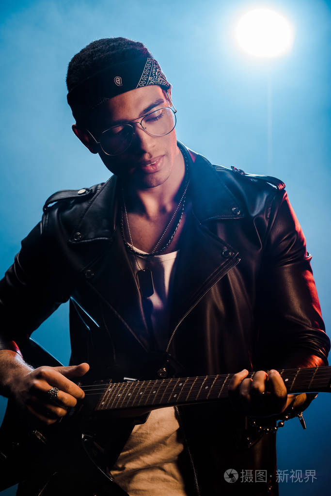 男摇滚明星穿着皮夹克,在舞台上用烟雾和戏剧灯光表演电吉他