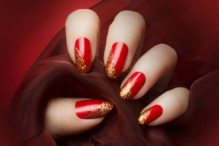 女性手与美丽的红色和金色闪闪发光的指甲，持有一个暗红色纺织红色背景指甲和指甲护理的概念。