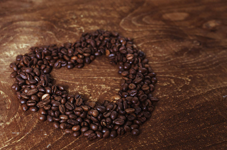 心形由咖啡豆在黑暗的木制背景上制成。 色调的乡村板。
