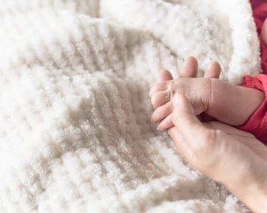 闭上母亲，手里握着婴儿的小手。 热爱温暖的关怀和安全的概念照片。 新出生的婴儿手，舒适的白色毛毯背景