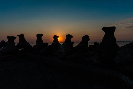 夕阳中的橙色太阳，海洋中有防波堤