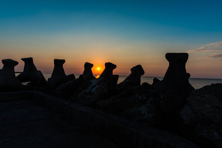 夕阳中的橙色太阳，海洋中有防波堤