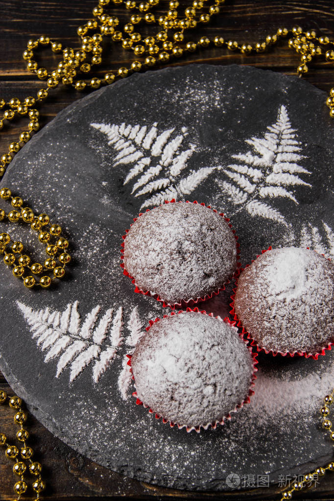 在黑暗的背景上的巧克力松饼与用糖粉画的小树枝装饰