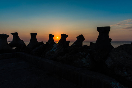 夕阳中的橙色太阳，海洋中有防波堤