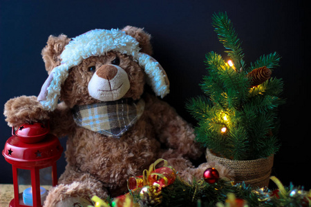 可爱的玩具熊拿着爪子在黑色背景上的红色灯笼上。 在框架里，你可以看到一棵有装饰品的小圣诞树。