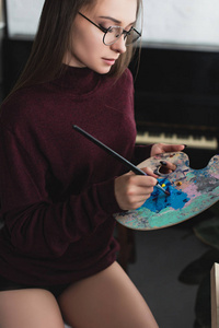穿着勃艮第毛衣的漂亮女孩坐着，手里拿着画笔调色板和绘画