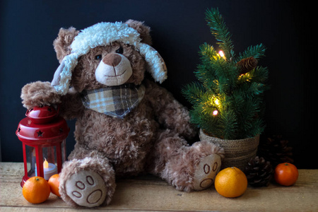 可爱的玩具熊拿着一只爪子在黑色背景上的红色灯笼上。在相框里，你可以看到一棵有装饰品的小圣诞树。