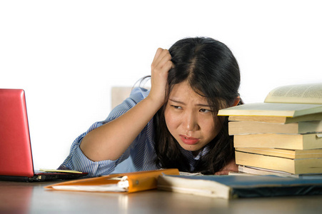 亚裔日本青少年学生努力工作,笔记本电脑和书籍堆在桌子上不知所措,精