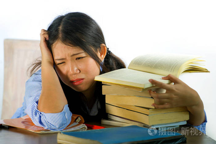 学生努力工作靠在笔记本上书堆在桌子上不知所措精疲力竭感到疲倦和