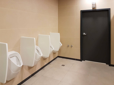 浴室内部采用浅米色和白色。 椭圆形陶瓷小便器。 男人需要的地方。 城市基础设施公共区域的洗手间。 公共空间的内部。