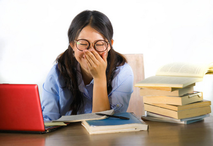 年轻甜美快乐的亚裔韩国学生女孩，戴着书呆子般的眼镜，在桌上的笔记本电脑上欢快地工作，一堆书在学习，在白色背景下微笑