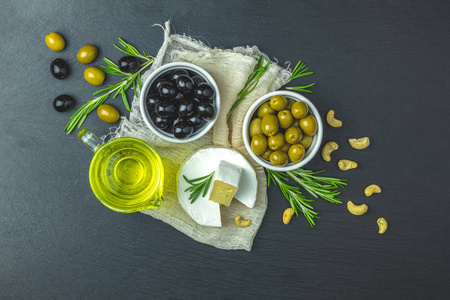 一套奶酪凸轮，黑色和绿色橄榄，盘子上的鹌鹑蛋，橄榄油和迷迭香，在黑色的石桌背景上。俯视图，复制空间..