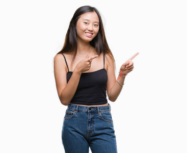 年轻的亚洲女人在孤立的背景上微笑着，看着相机，用两只手和手指指向一边。