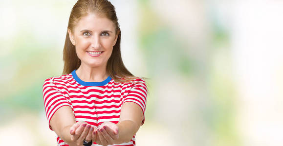 中年成熟的女人穿着休闲的t恤，在孤立的背景上微笑，双手掌心一起接受或给予手势。持有和保护
