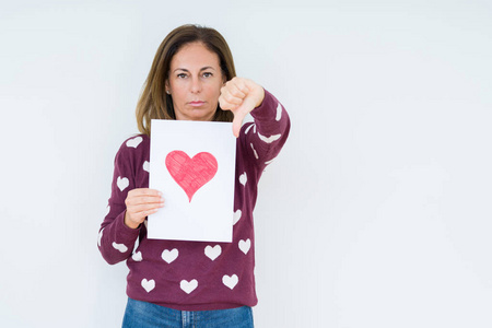 中年妇女拿着红心卡礼物，脸上带着愤怒的孤立的背景，消极的信号，用拇指向下显示不喜欢，拒绝的概念