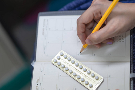 口服避孕药与女性手书写时间表水泡的避孕药。 堕胎概念。