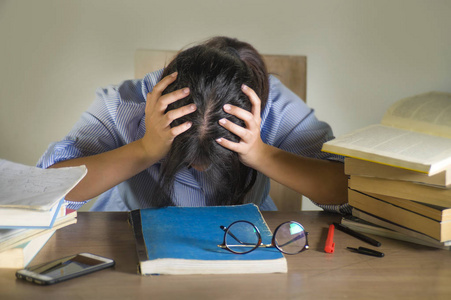 年轻沮丧,压力大的女学生在笔记本电脑和书堆旁工作,备考时不知所措