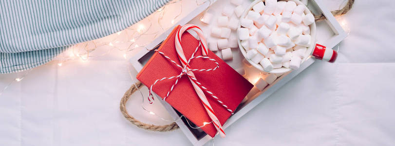 新年或圣诞节平躺顶景与热可可咖啡巧克力与棉花糖杯圣诞节庆祝红色礼物盒在木制托盘在床上与灯。 2019年长宽旗帜