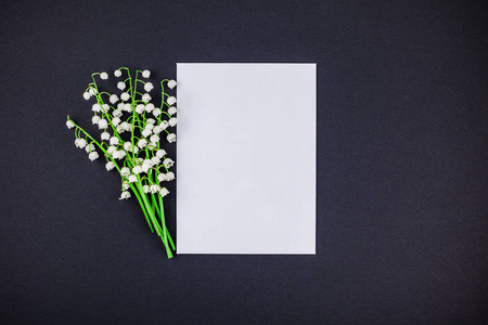 创造性的平躺顶部视图模拟与新鲜的百合花的山谷在一个黑色的纸背景与空白的白色字母框架和复制空间在最小的风格模板的文本。