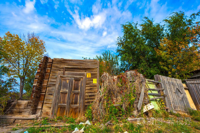 一座破旧的破旧房子里只有一扇木门和棕色的篱笆上面长满了绿色的