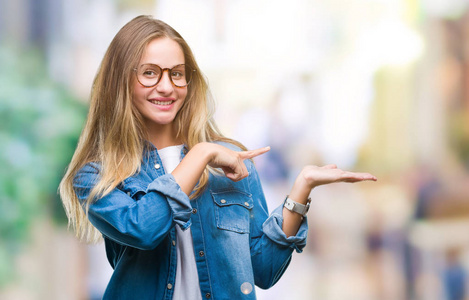 年轻漂亮的金发女人戴着眼镜在孤立的背景上惊讶和微笑的相机，同时呈现手和手指。