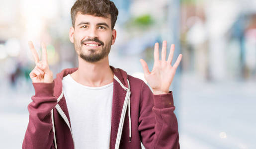 年轻的英俊男子在孤立的背景显示和指向7号手指，同时微笑自信和快乐。