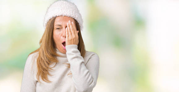 美丽的中年妇女穿着冬季毛衣和帽子，在孤立的背景上打哈欠，疲倦地用手遮住半张脸眼睛和嘴巴。 脸疼。