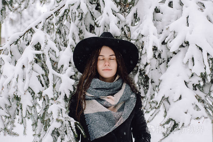 一个戴着帽子的女孩的肖像，她站在树枝下，下雪了