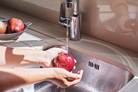 女人在厨房的金属水槽里洗红苹果