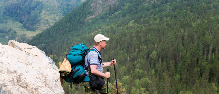 高山上的游客看大自然。 一个背着背包的人坐在一块大石头上，看着风景。