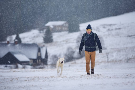 宠物主人和他的狗之间的友谊。 在冬天的风景中，年轻人带着拉布拉多猎犬散步。 捷克共和国吉萨山脉