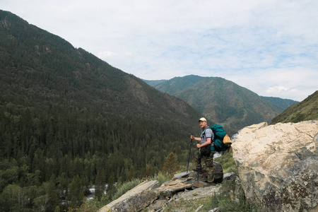高山上的游客看大自然。 一个背着背包的人坐在一块大石头上，看着风景。