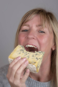 金发女人在吃和享受一块蓝色奶酪