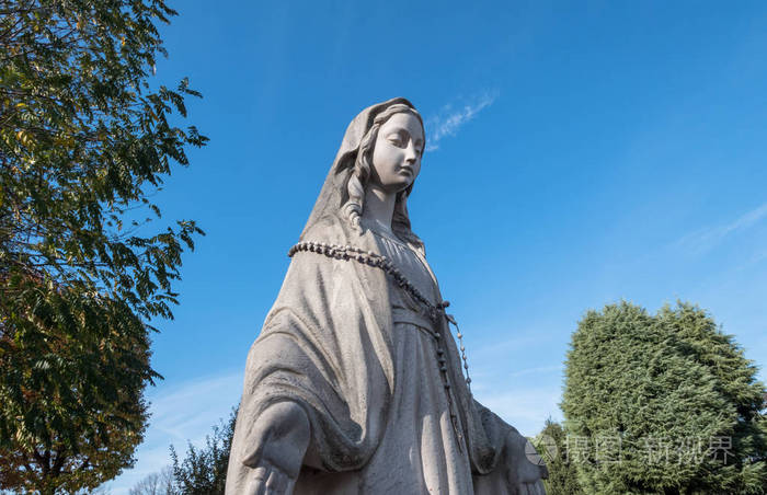 圣母玛利亚雕像张开双臂背景是蓝天和绿树理想的概念和节日