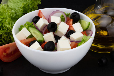 希腊沙拉与新鲜蔬菜，菲塔奶酪和黑色橄榄在黑暗的背景。