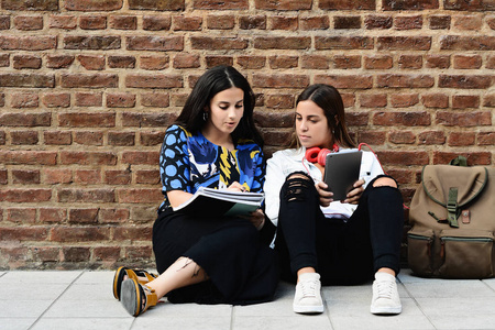两名女学生正在准备考试与工作簿和平板电脑在城市背景。 教育观念。