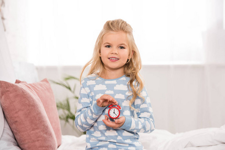 幸福可爱的孩子坐在床上，手里拿着小钟