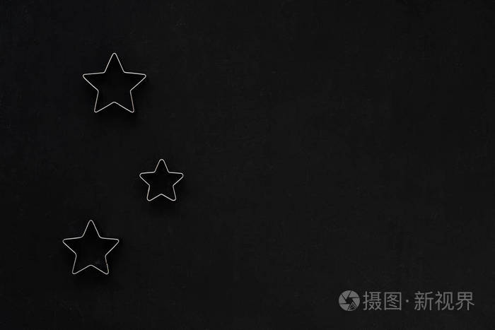 黑色节日背景上的金属星星烘焙模具饼干切割机平躺式顶部视图