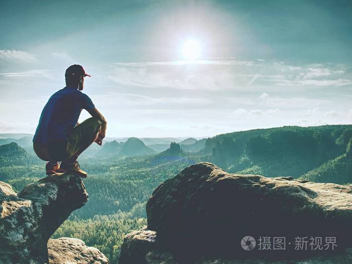 穿着蓝色黄色运动服的人坐在锋利的悬崖上,欣赏远景.