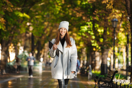 一个红头发的快乐女人在街上散步的照片，微笑着拥抱笔记本电脑。