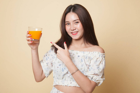 年轻的亚洲女人指着米色背景的橙汁