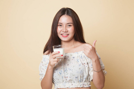 健康的亚洲女人喝着一杯牛奶，在米色背景下竖起大拇指
