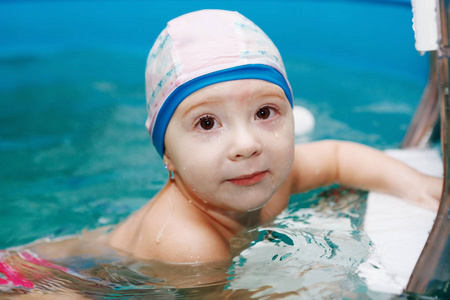 婴儿坐在游泳池里的楼梯上玩球。 健康的生活方式。 水疗。 游泳康复。