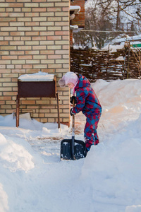 快乐的女孩用铲子挖雪，建造雪隧道。 冬季户外游戏。