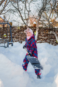 快乐的女孩用铲子挖雪，建造雪隧道。 冬季户外游戏。