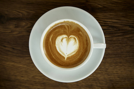 一杯带有心形图案的咖啡，放在白色的杯子里，背景是乡村木制的，有着美丽的拿铁艺术
